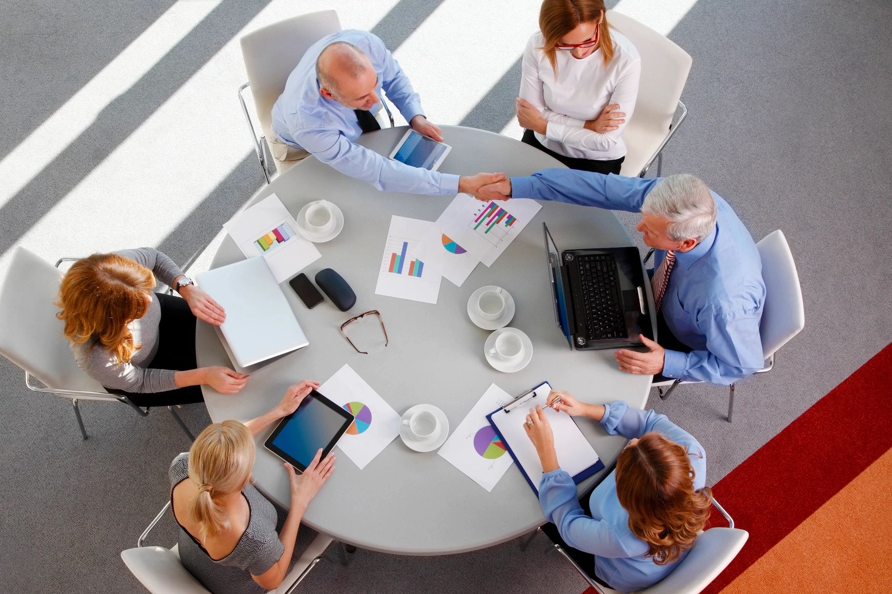 overhead view of a business meeting. laptops, reports, and cups scattered on the table.