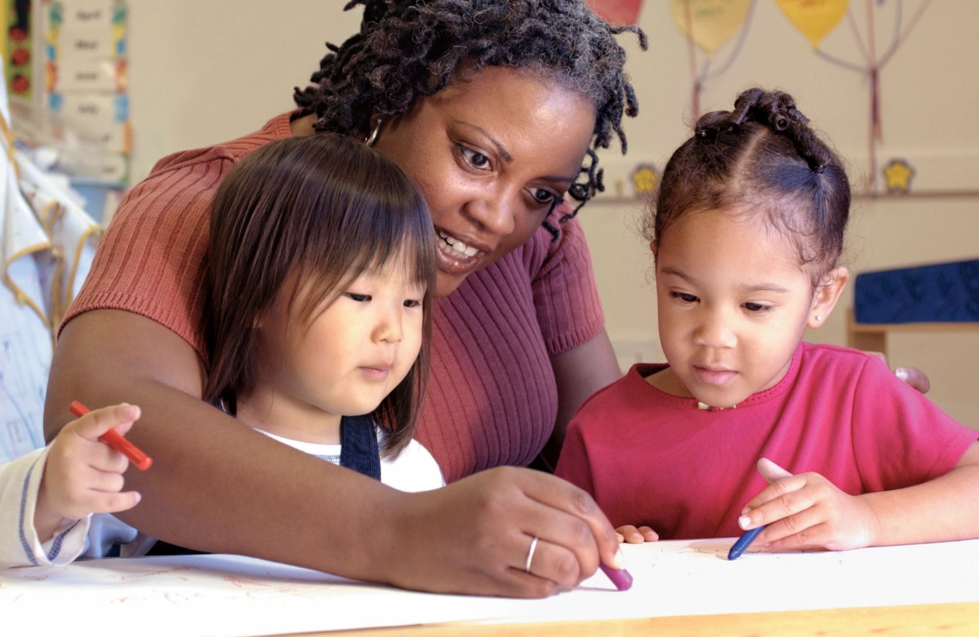 Photo of teacher helping two children with classwork